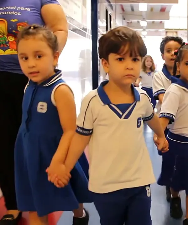 Crianças do Infantil de mãos dadas atravessando o corredor da escola
